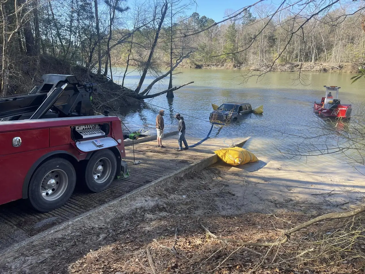 Crew recovering a submerged SUV from a river boat ramp using recovery airbags