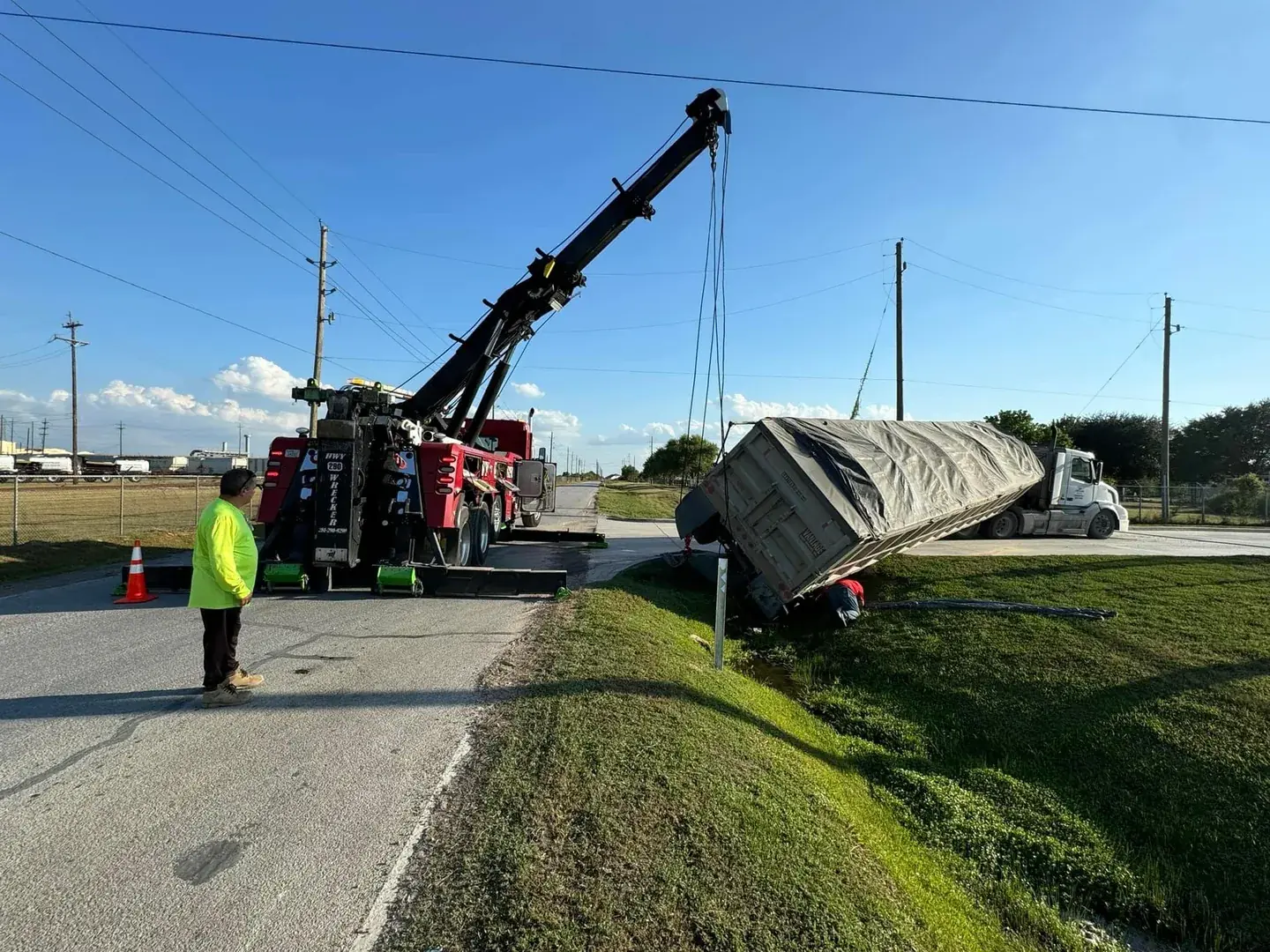 HWY 290 Wrecker uprighting an overturned tarped trailer on a rural Texas road
